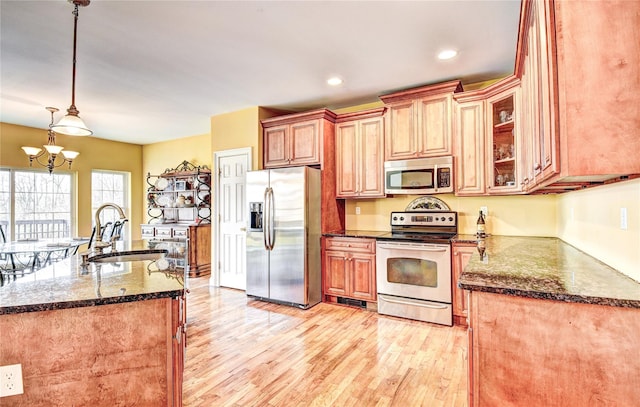 kitchen with pendant lighting, dark stone counters, sink, appliances with stainless steel finishes, and light hardwood / wood-style floors