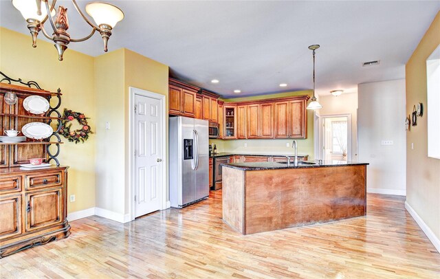 kitchen with sink, stainless steel appliances, light hardwood / wood-style floors, decorative light fixtures, and a center island with sink