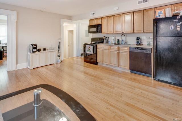 kitchen with sink, black appliances, light brown cabinets, and light wood-type flooring