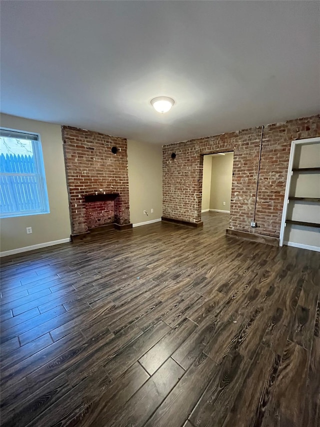 unfurnished living room with dark hardwood / wood-style flooring, brick wall, and a brick fireplace