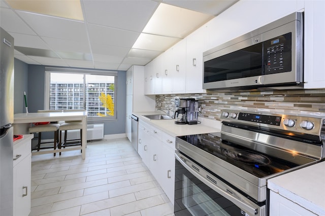 kitchen featuring a paneled ceiling, tasteful backsplash, stainless steel appliances, sink, and white cabinetry