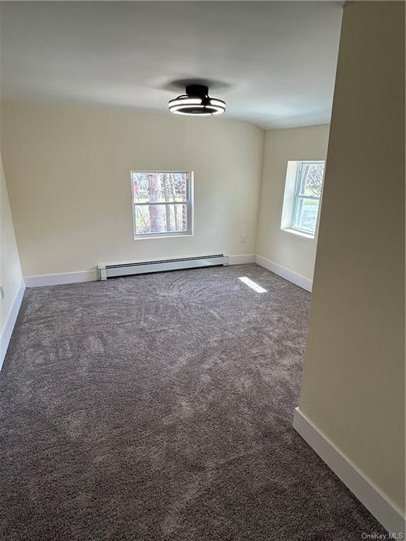 unfurnished room with a wealth of natural light, dark carpet, and baseboard heating