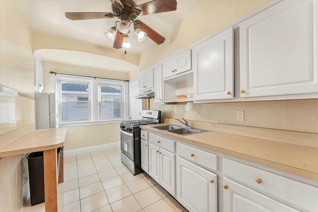 kitchen featuring sink, gas range, decorative backsplash, light tile patterned floors, and white cabinetry