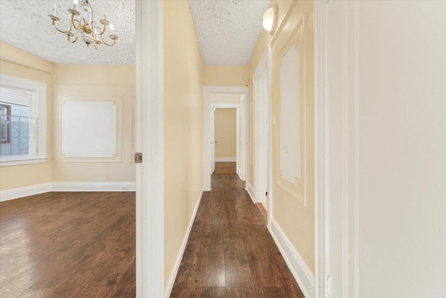 hallway featuring dark hardwood / wood-style flooring, a textured ceiling, and an inviting chandelier