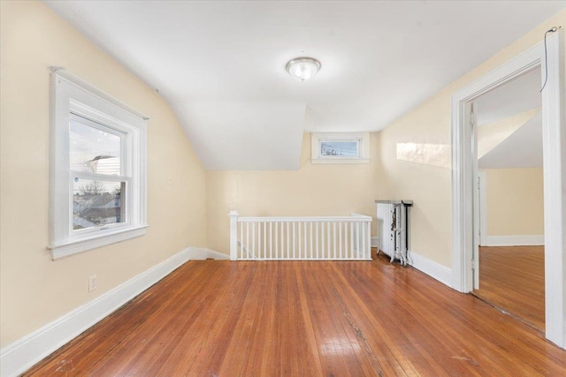 additional living space with hardwood / wood-style flooring, lofted ceiling, and radiator heating unit