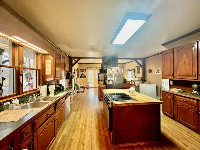 kitchen with sink, a skylight, a kitchen island, appliances with stainless steel finishes, and light hardwood / wood-style floors