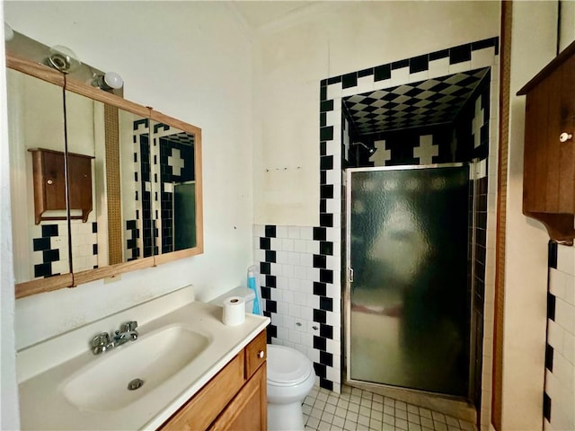 bathroom with tile patterned floors, toilet, a shower with door, vanity, and tile walls