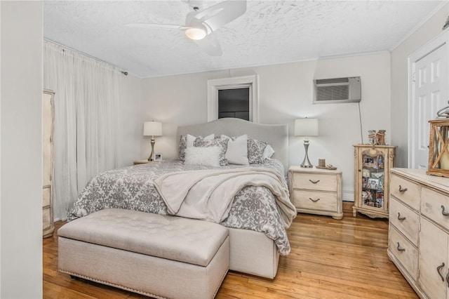 bedroom with a wall mounted AC, ceiling fan, light hardwood / wood-style floors, and a textured ceiling