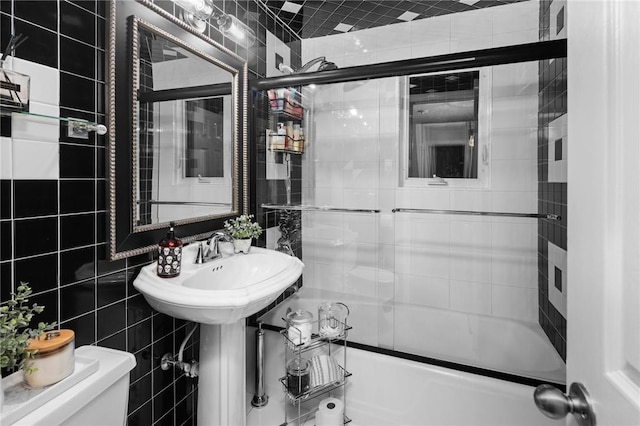 bathroom with toilet, bath / shower combo with glass door, and tile walls