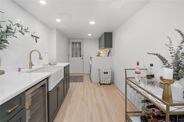 kitchen with light wood-type flooring, washer / clothes dryer, wine cooler, and sink