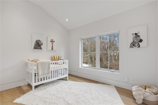 bedroom with a nursery area, lofted ceiling, and wood-type flooring