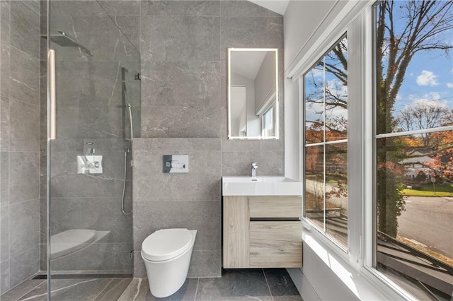 bathroom with a tile shower, vanity, tile walls, and toilet