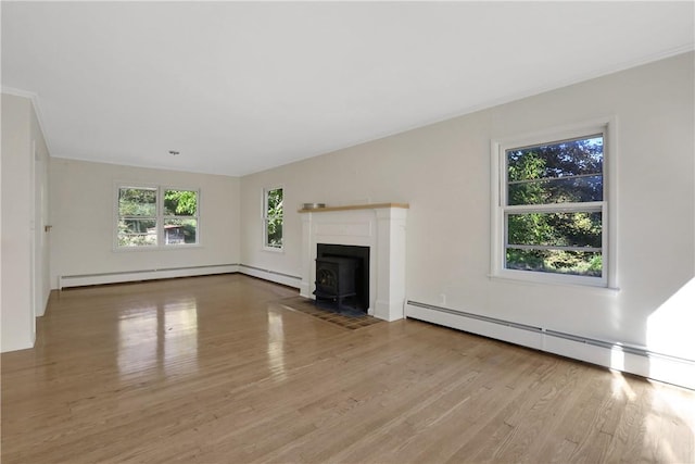 unfurnished living room featuring a wood stove, plenty of natural light, a baseboard radiator, and light wood-type flooring