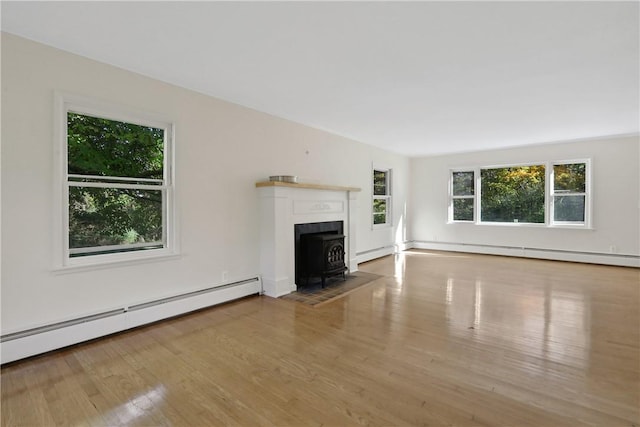 unfurnished living room with light hardwood / wood-style floors, a wood stove, and a baseboard heating unit