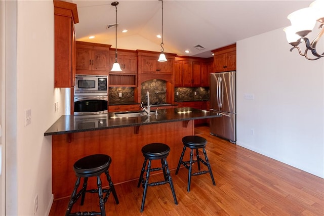 kitchen with backsplash, sink, light hardwood / wood-style flooring, appliances with stainless steel finishes, and decorative light fixtures