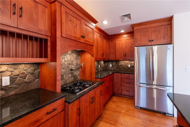 kitchen with black gas cooktop, backsplash, dark stone countertops, stainless steel fridge, and light hardwood / wood-style floors