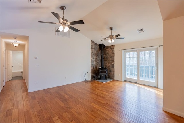 unfurnished living room with a wood stove, ceiling fan, light hardwood / wood-style flooring, and vaulted ceiling