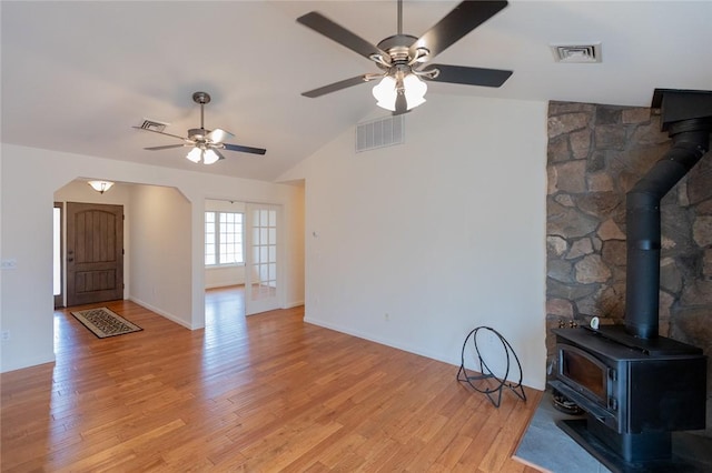 unfurnished living room featuring a wood stove, light wood-type flooring, vaulted ceiling, and ceiling fan