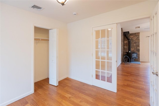 unfurnished bedroom featuring a wood stove, a closet, and light wood-type flooring