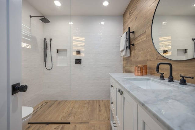 bathroom with vanity, tiled shower, wood-type flooring, tile walls, and toilet