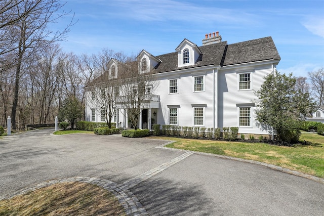 colonial house featuring a chimney, a balcony, and a front yard
