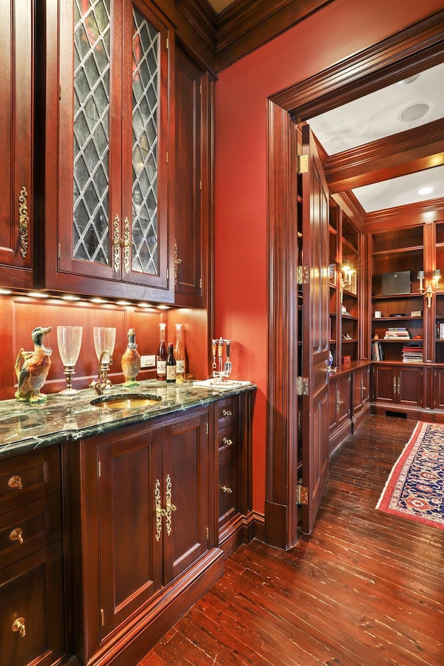 bar featuring a sink, dark wood finished floors, built in features, indoor wet bar, and ornamental molding
