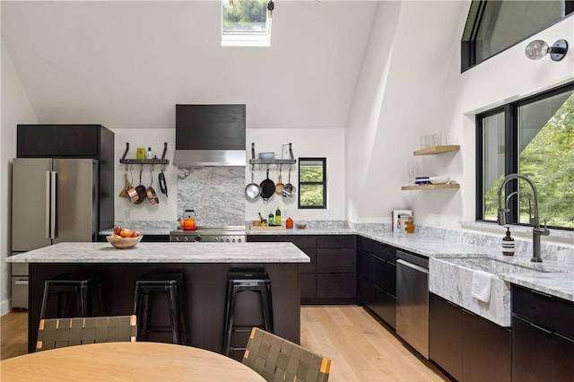 kitchen with a wealth of natural light, vaulted ceiling with skylight, wall chimney exhaust hood, and stainless steel appliances