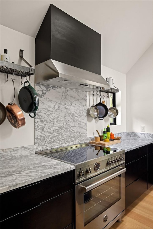 kitchen with high end stove, wall chimney exhaust hood, and light wood-type flooring