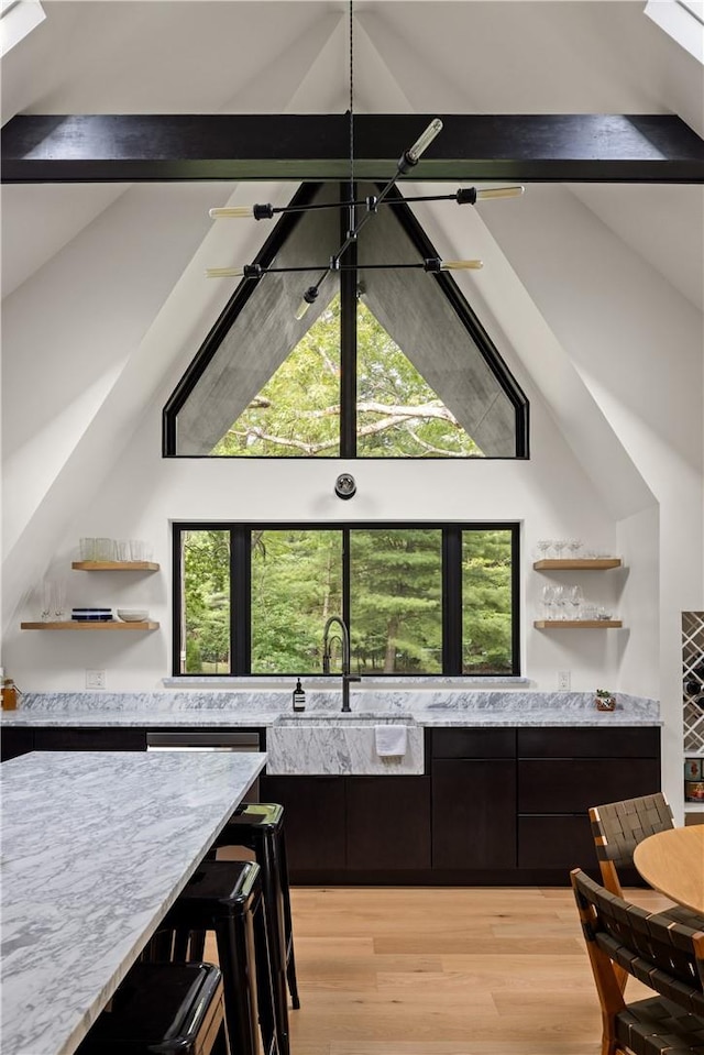 kitchen featuring vaulted ceiling with beams, light stone counters, sink, and light hardwood / wood-style floors