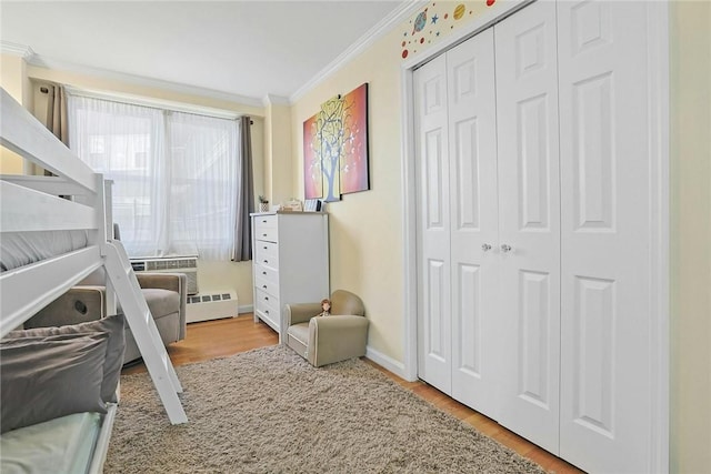 bedroom with a baseboard heating unit, light hardwood / wood-style floors, a closet, and crown molding