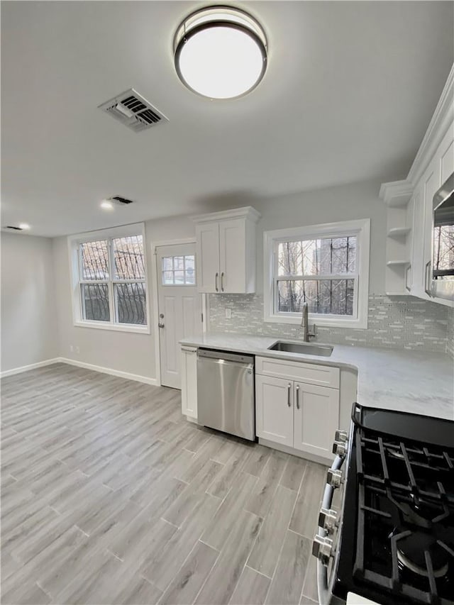 kitchen featuring visible vents, stainless steel appliances, light countertops, open shelves, and a sink