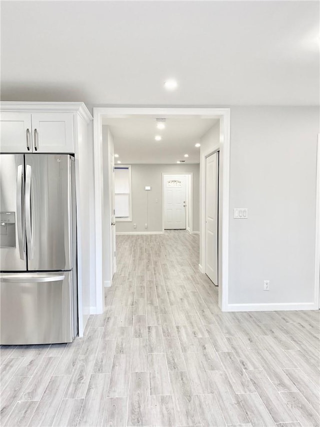 kitchen with light wood-style floors, stainless steel fridge, baseboards, and white cabinets