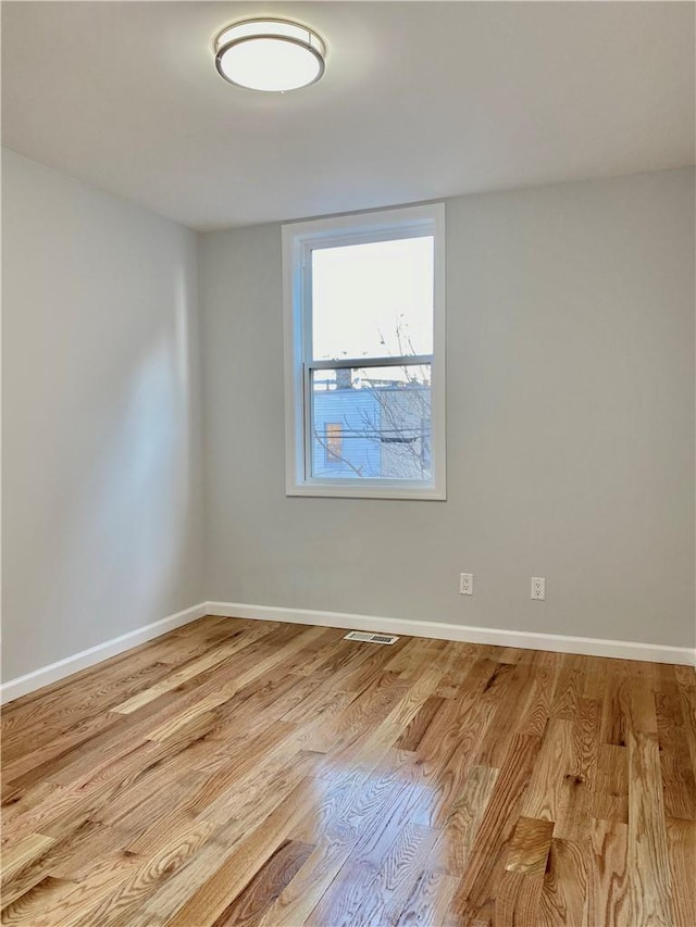 unfurnished room featuring light wood finished floors, visible vents, and baseboards