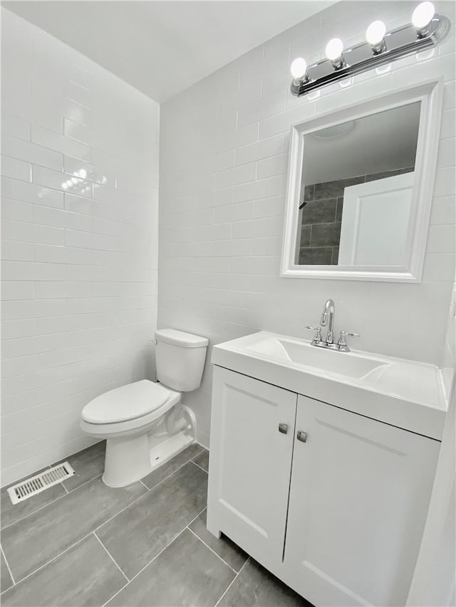 bathroom with visible vents, tile walls, toilet, and vanity