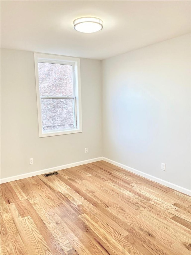 empty room featuring light wood-type flooring, visible vents, and baseboards