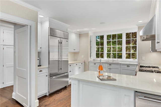 kitchen with stainless steel built in refrigerator, sink, extractor fan, white cabinetry, and light stone countertops