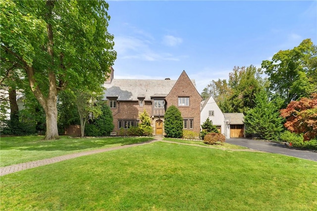 english style home featuring brick siding, driveway, and a front lawn