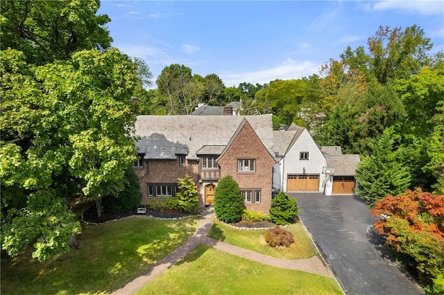 tudor house with aphalt driveway, a chimney, and a front lawn