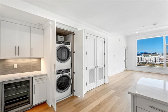 washroom with light hardwood / wood-style flooring, beverage cooler, stacked washer and clothes dryer, and ornamental molding