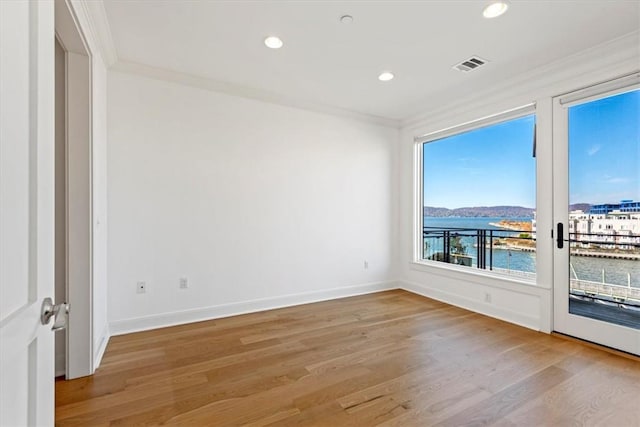 spare room with crown molding, recessed lighting, a water view, visible vents, and light wood-style flooring