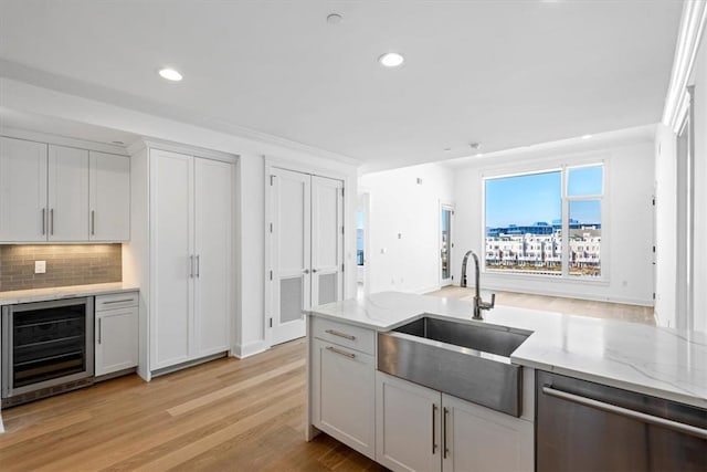 kitchen with beverage cooler, a sink, white cabinetry, stainless steel dishwasher, and light stone countertops