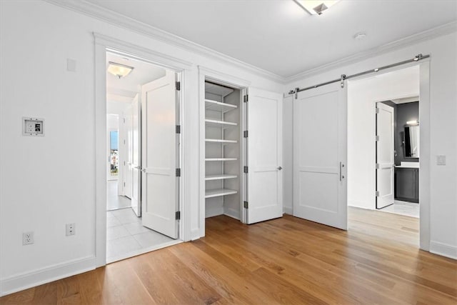 unfurnished bedroom with a barn door, ornamental molding, and light wood-style flooring