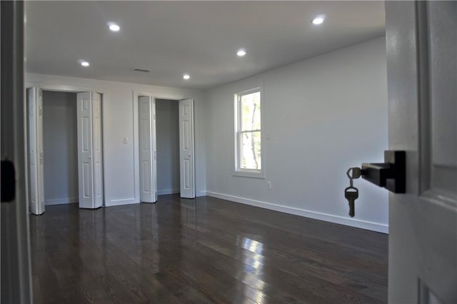 unfurnished bedroom with multiple closets and dark wood-type flooring