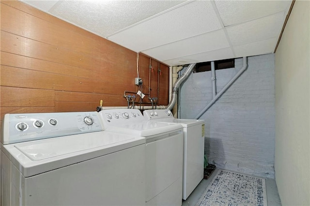 washroom featuring separate washer and dryer, wooden walls, and brick wall