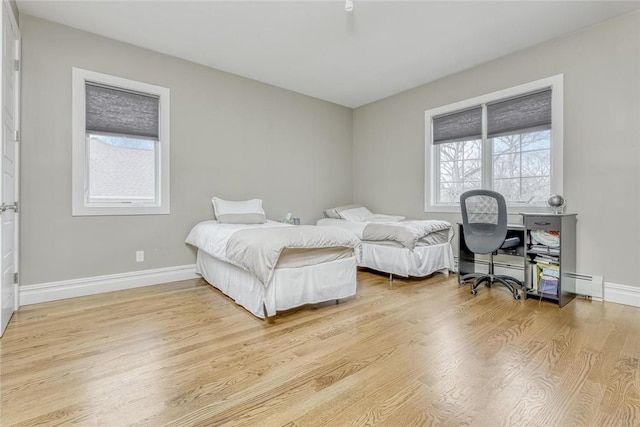 bedroom featuring multiple windows, light hardwood / wood-style floors, and a baseboard heating unit