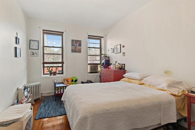 bedroom featuring radiator heating unit, cooling unit, and wood-type flooring