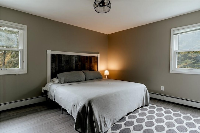 bedroom with multiple windows, a baseboard radiator, and hardwood / wood-style flooring