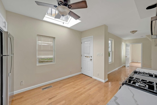 kitchen with light stone countertops, stainless steel fridge, light wood-type flooring, ceiling fan, and white range with gas stovetop