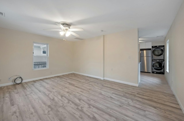 unfurnished room featuring stacked washer and dryer, light hardwood / wood-style flooring, and ceiling fan