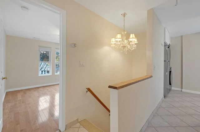 hallway with a chandelier, stacked washing maching and dryer, and light hardwood / wood-style floors